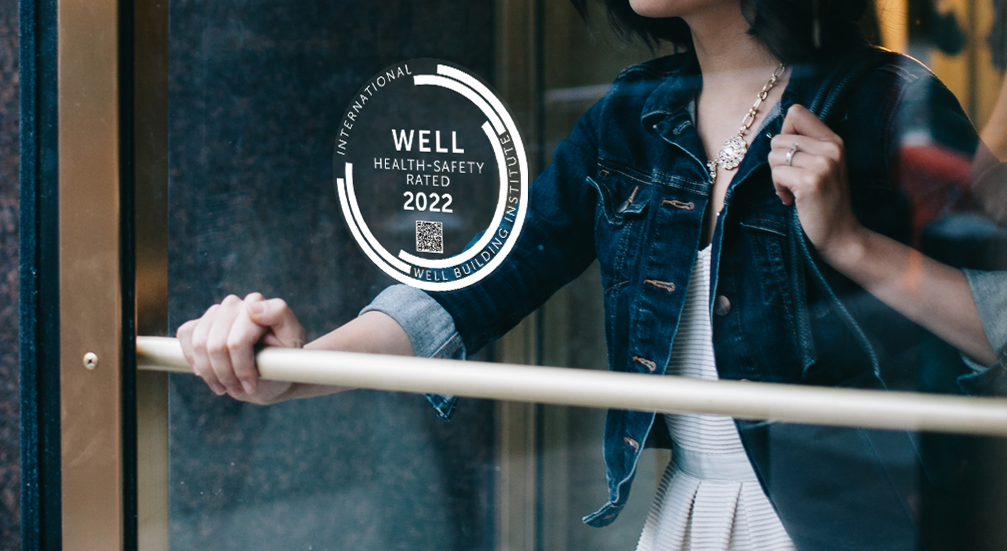 A glass door bears the WELL Health-Safety Rated 2020 seal, including a QR code for visitors to learn more